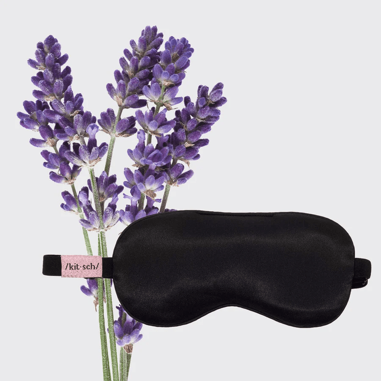 Black satin weighted eye mask beside fresh purple lavender flowers