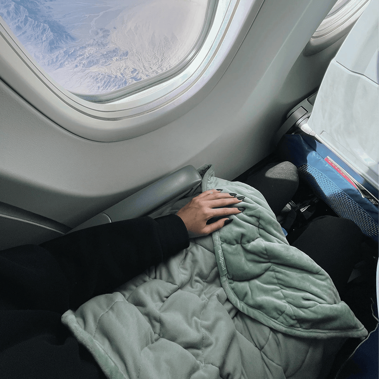 Sage green weighted wearable blanket used as lap blanket in airplane cabin